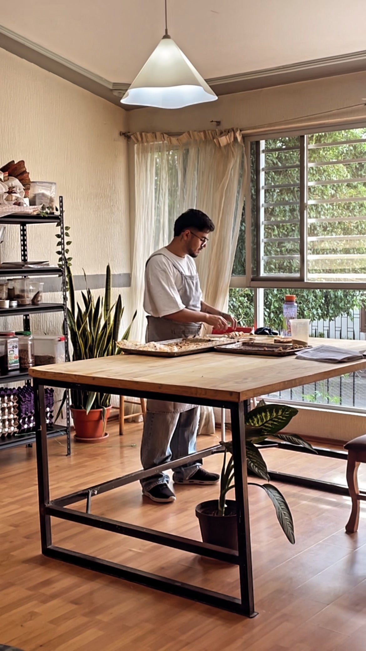 Agustín preparando comida junto a la ventana y las plantas de la casa
